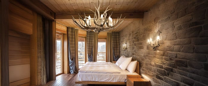 The image depicts a white chandelier hanging over a bed in a bright, minimalistic bedroom. The chandelier features multiple curved arms with candle-like bulbs, creating a classic and elegant look, perfect for bedroom lights.