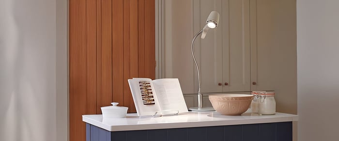 Minimalist kitchen island with a modern task lamp, open cookbook, and wooden bowl against warm and neutral cabinetry.