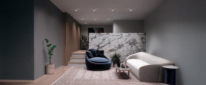 Minimalist living room with recessed ceiling living room lights, marble partition wall, velvet chair, and neutral-toned curved sofa.