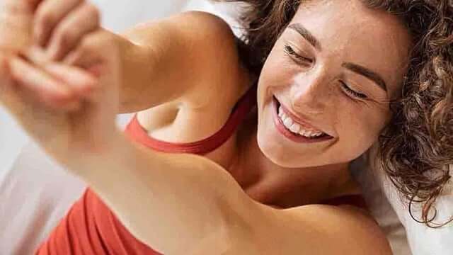 Illustration of a person who wake up sweaty in a hot bedroom, sitting on the bed with a fan running and visible heat waves in the air.