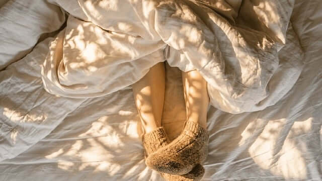 person under a blanket with warm socks, showing cold sleeper needing the best warm comforter for cold sleepers