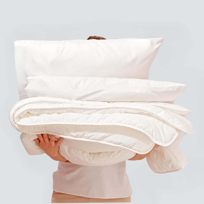 Stack of pillows and a folded duvet displayed together, representing the warmest winter comforter for cozy seasonal bedding.