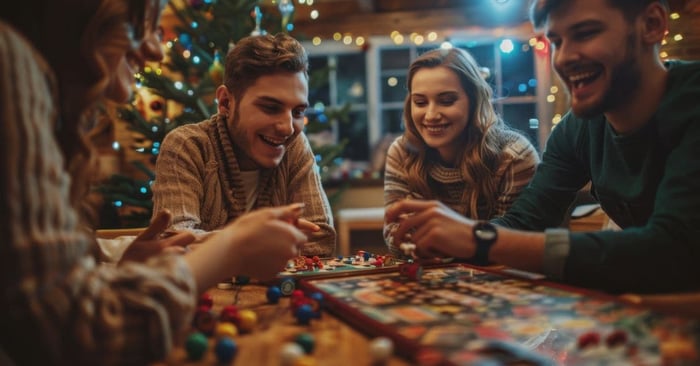 Group of four young men and women sitting at a table and laughing while playing a Christmas party game