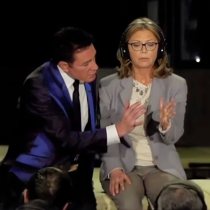 Distance healing demonstration on stage, woman seated with hands raised responding to subtle interaction while Dr. Eric Pearl observes closely without touching