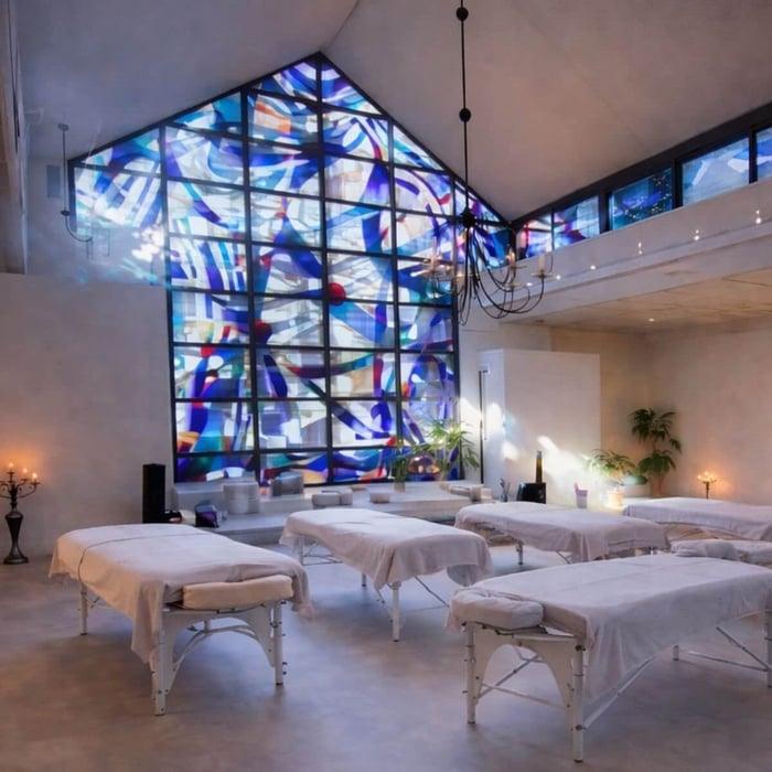 Healing environment inside Blue Rose Bloemendaal, featuring a calm, light-filled space with white massage tables, soft lighting, and a blue stained-glass window supporting awareness and receivership in Reconnective Healing®.