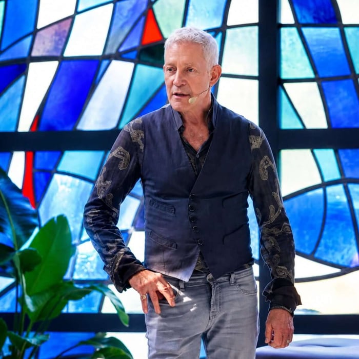 Dr. Eric Pearl presenting healing frequencies during a live demonstration in the Netherlands, standing before a stained-glass backdrop and sharing insights on Reconnective Healing® with an engaged audience.