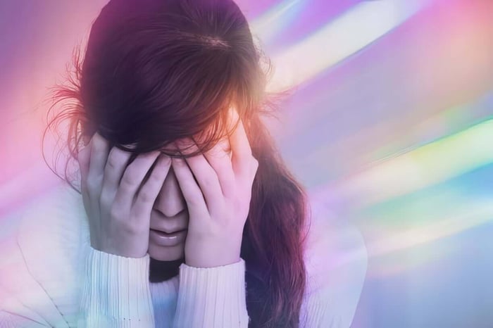 Woman covering face with hands against colorful light streaks