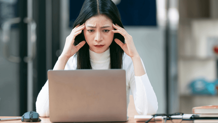 Woman holding head in stress while working on laptop