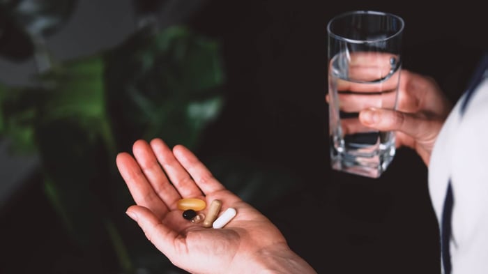Hand holding supplements with other hand holding a glass of water
