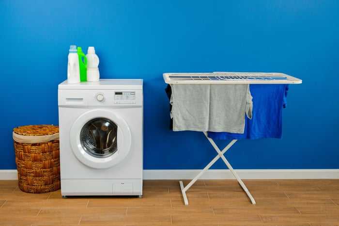 Laundry room with a front-loading washing machine, detergent bottles, and a drying rack with clothes — ideal setup for homes using an indoor clothes dryer vent.