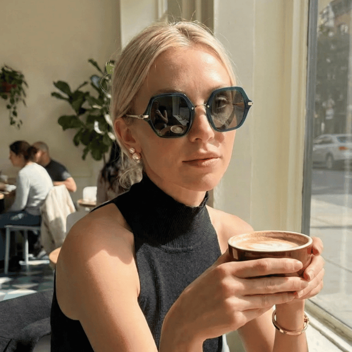 Best sunglasses for women with small faces worn by a woman in a sunlit café, featuring structured green frames that complement petite facial proportions.