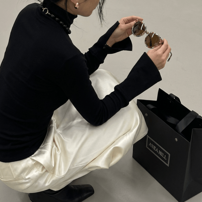Luxury brand purpose, woman holding ANEA HILL Tahoe sunglasses in floral Italian cellulose acetate alongside a black ANEA HILL shopping bag