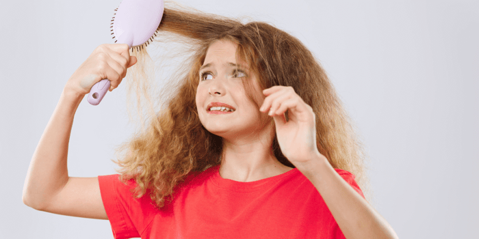 A young girl brushing her tangled hair, illustrating the need for a detangler spray and the benefits of choosing a non toxic detangler and safe children’s detangler