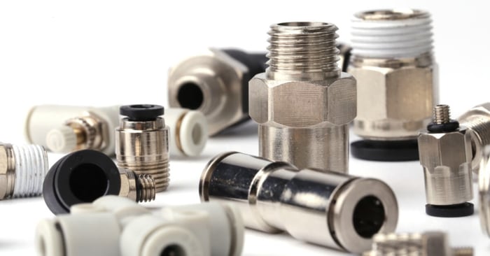 Assorted metal and plastic pneumatic fittings with threaded ends and push-to-connect ports arranged on a white surface.