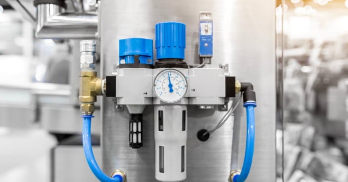 Compressed air filter regulator assembly with pressure gauge and blue air lines mounted on industrial processing equipment.