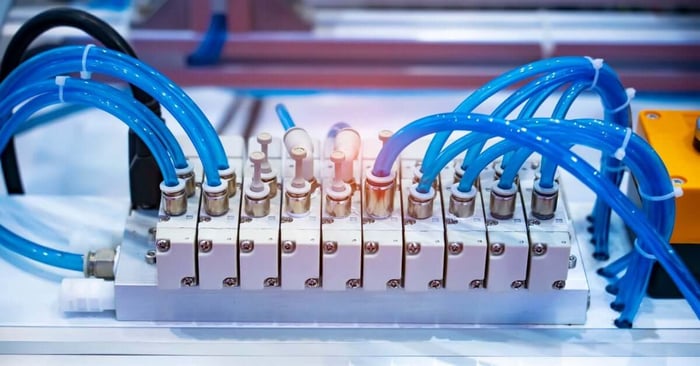 A close-up of a white pneumatic system consisting of several blue hoses connected to a valve controller.