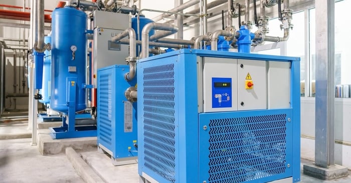 A blue refrigerated air dryer with a control panel on the side and multiple pipes connected to the unit.