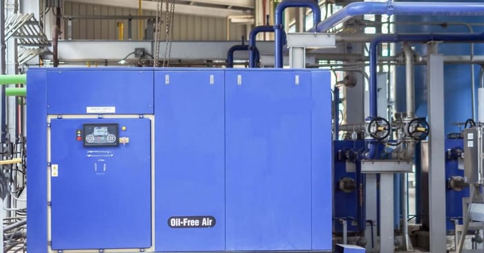 A large blue air compressor system with a control panel on the front and multiple pipes in the background.