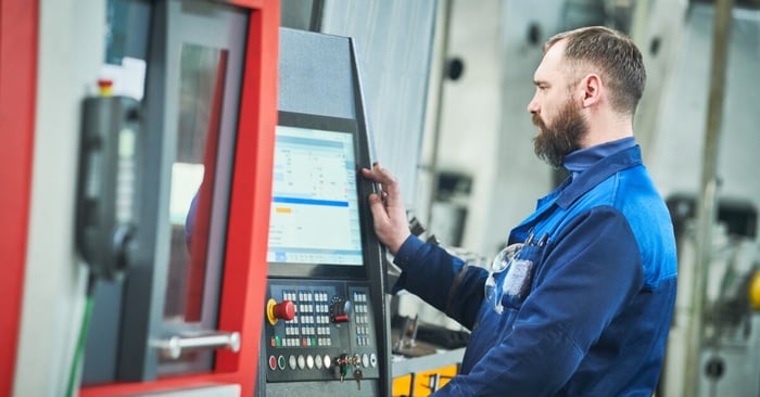 A CNC machine operator in blue workwear using a control panel beside a large industrial machining center.