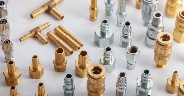 Assorted brass and steel pneumatic hose fittings, couplers, and barbed connectors arranged on a white tabletop.