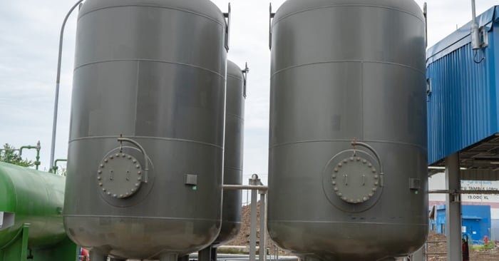Large gray vertical air receiver tanks installed outdoors beside industrial piping on an overcast day.