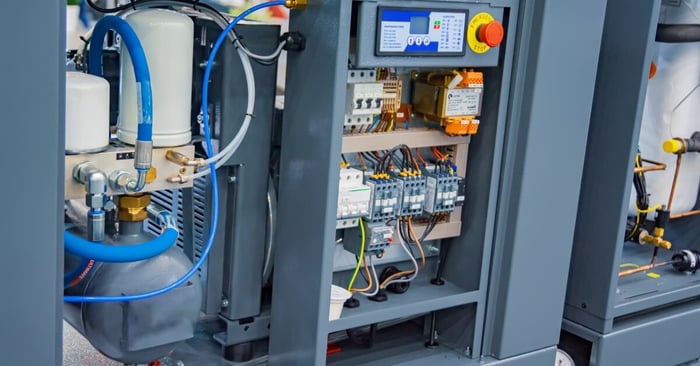 An industrial air compressor system with a filtration unit, blue hoses, and an open electrical control panel.