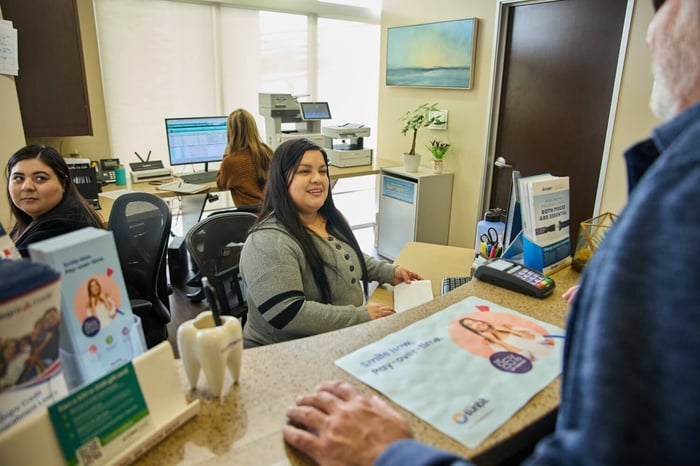 Friendly dental front desk staff assisting a patient at the reception counter inside a modern dental office.