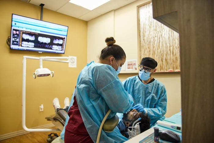 Dentists wearing protective gear performing a dental procedure in a modern treatment room.