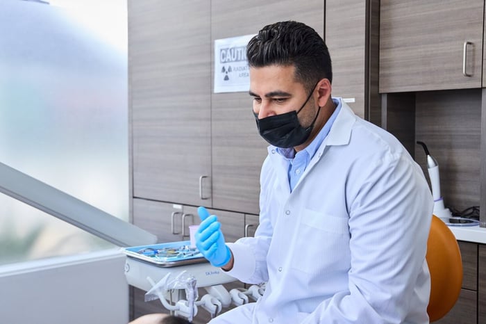 A dentist wearing a white robe and a face mask