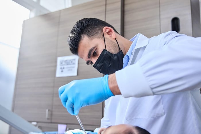 A person wearing a white scrub and a face mask