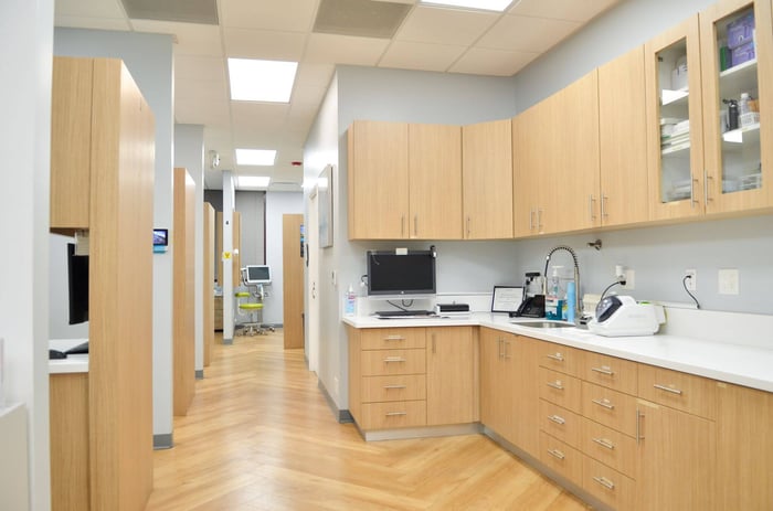 Clean dental office hallway with light wood cabinetry, countertops, and clinical workstations.
