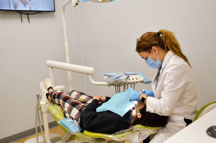 Dentist wearing a mask and gloves providing dental care to a patient reclined in a treatment chair.