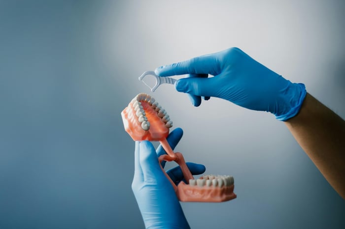 A hand flossing a dental model