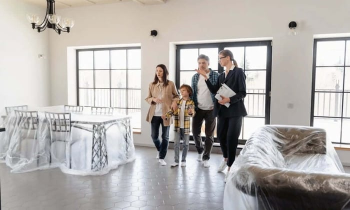 Family touring a vacant home with covered furniture, where a cellular temperature monitor helps property owners prevent damage between tenants