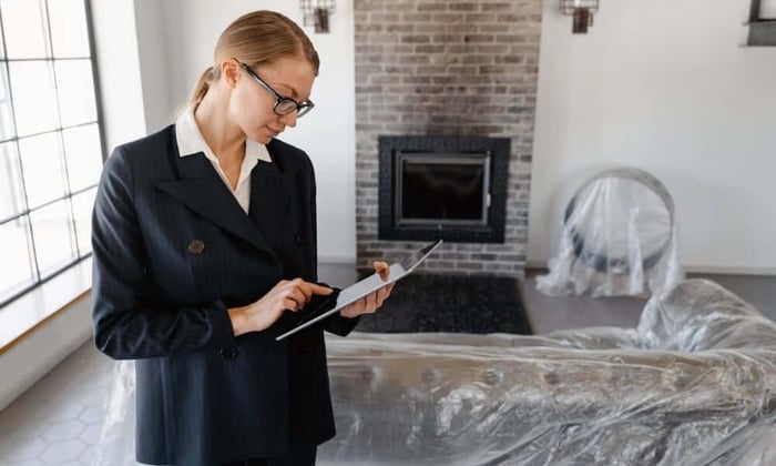 Property manager using tablet to check WiFi vs cellular monitoring alerts in vacant home with covered furniture