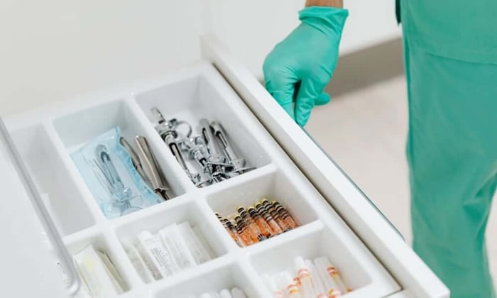Healthcare worker in gloves accessing medication and supply storage drawer in a small clinic, where temperature monitoring in healthcare facilities protects inventory from power outages.