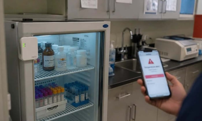 Laboratory refrigerator temperature monitoring setup in a small lab, tracking reagent and specimen storage with a cellular sensor.