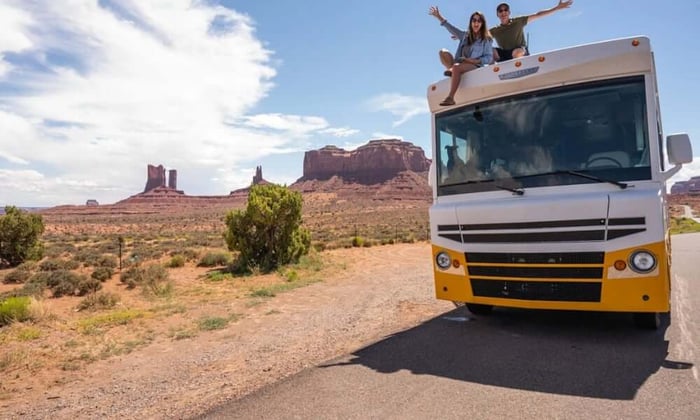 Couple celebrating on top of an RV in Monument Valley desert, pet monitoring keeps your animals safe while you explore the road.