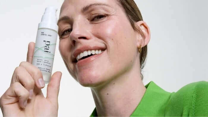 Smiling woman in bright green top holding Pai Age Confidence serum, showcasing the anti-aging skincare product