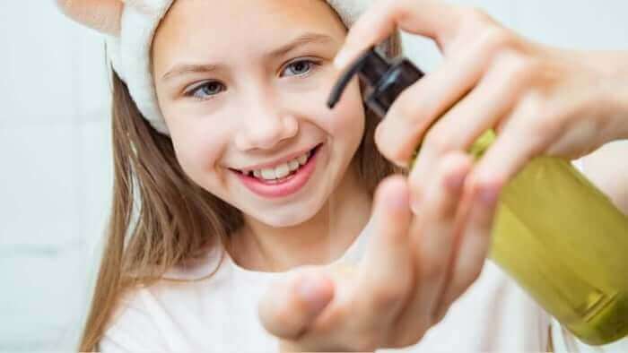 Smiling tween girl with headband applying golden serum from dropper bottle to her palm during skincare routine