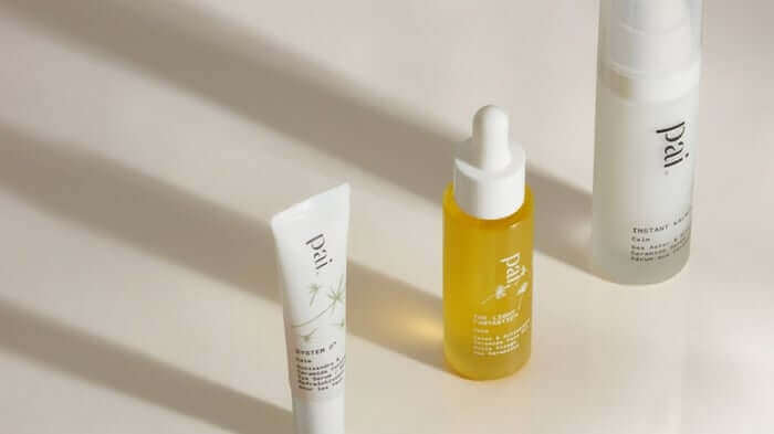 Three Pai Skincare products arranged on white surface with natural shadows - white tube, golden yellow Rosehip BioRegenerate Oil serum, and white spray bottle for sensitive skin care