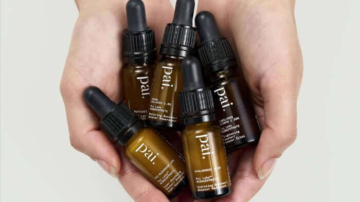 Hands holding five amber glass dropper bottles of Pai face oils and serums with black droppers, natural skincare for sensitive skin