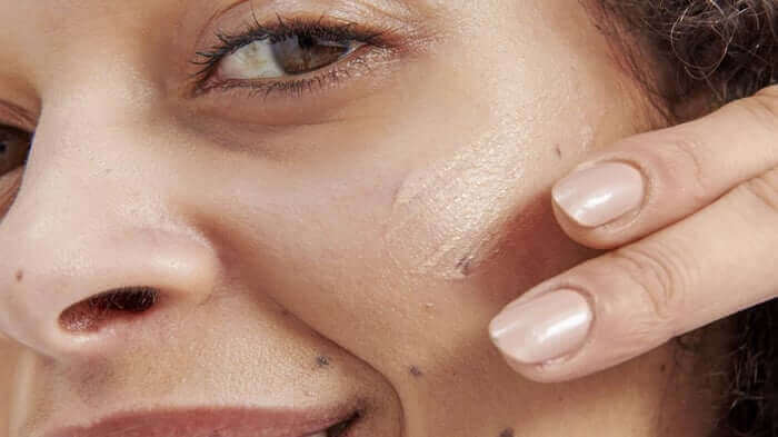 Teen applying facial serum to cheek with fingertip, showing healthy glowing skin and natural skincare routine