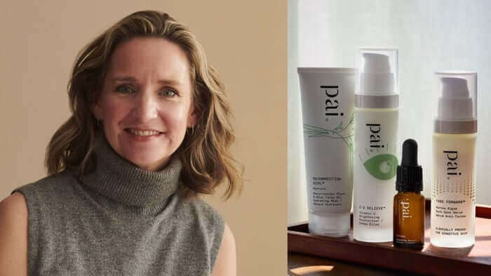 Woman with blonde wavy hair wearing grey turtleneck next to Pai Skincare products including Resurrection serum and Age Confidence oil on wooden surface