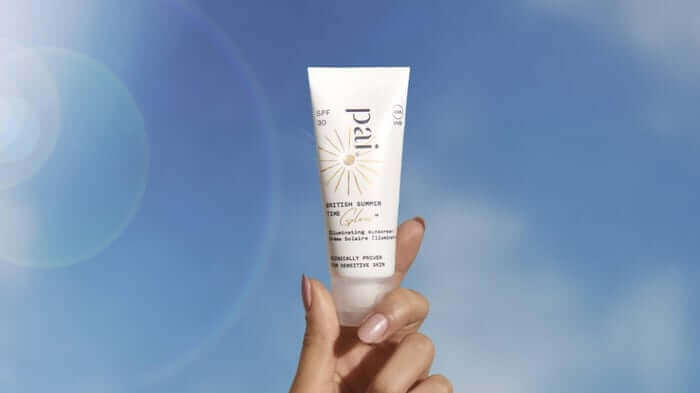 Hand holding Pai British Summer Time SPF 30 sunscreen tube against bright blue sky background