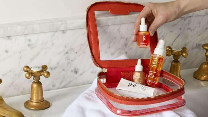 Hand selecting Rosehip BioRegenerate Oil from red leather Pai discovery set on marble bathroom counter with brass taps