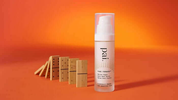 Pai Fade Forward serum bottle with pump dispenser on orange background next to wooden dominoes, targeting dark spots and hyperpigmentation