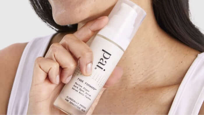 Woman holding Pai Skincare Fade Forward serum bottle against her neck, showing the lightweight liquid foundation product for sensitive skin