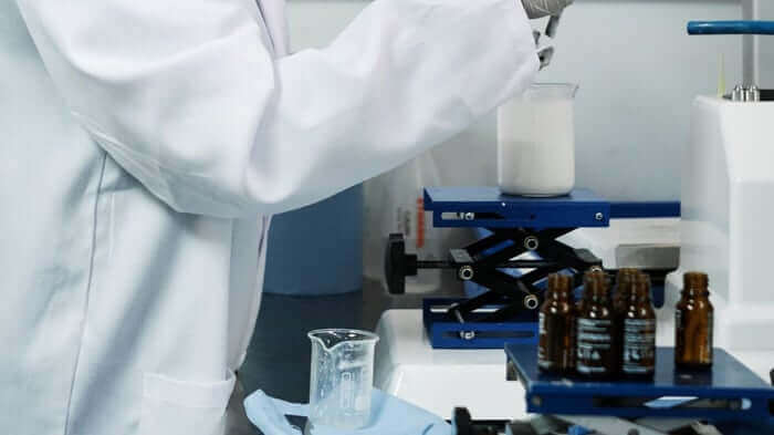 Lab technician in white coat working with brown glass bottles and scientific equipment in sterile laboratory setting