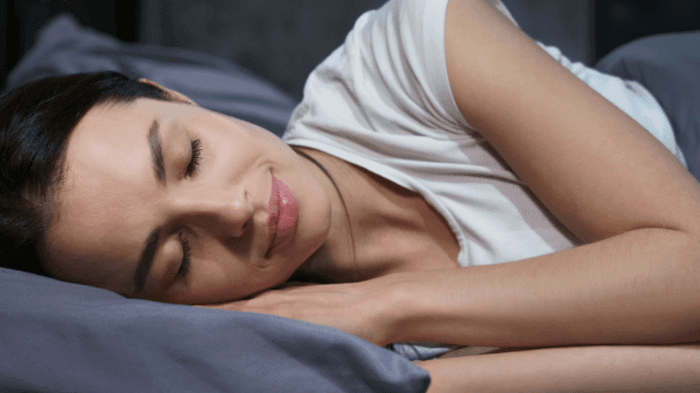 Woman sleeping peacefully in bed with clear, healthy skin showcasing the benefits of quality nighttime rest for skin repair